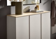 Modernes Sideboard mit drei weißen Fronten und heller Holzplatte, dekoriert mit Vase, Büchern und Lampe, in schräger Frontansicht von links.