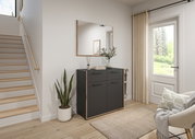 Moderne schwarze Kommode mit Holzrahmen und vier Türen im Flur, darüber ein rechteckiger Wandspiegel; seitliche Frontansicht in einem hellen Eingangsbereich neben Treppe und Fenster.