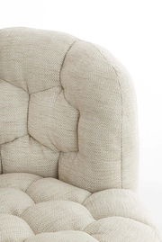 Nahaufnahme einer beigen, gepolsterten Couch mit strukturierter Oberfläche und Knopfheftung, seitliche Perspektive