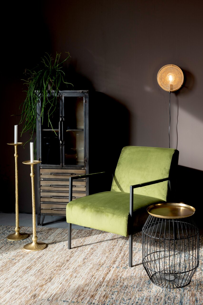 Highboard aus Metall mit Glastüren, dekoriert mit einer Pflanze, im Vordergrund ein grüner Sessel und ein Beistelltisch, seitliche Perspektive