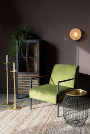 Highboard aus Metall mit Glastüren, dekoriert mit einer Pflanze, im Vordergrund ein grüner Sessel und ein Beistelltisch, seitliche Perspektive