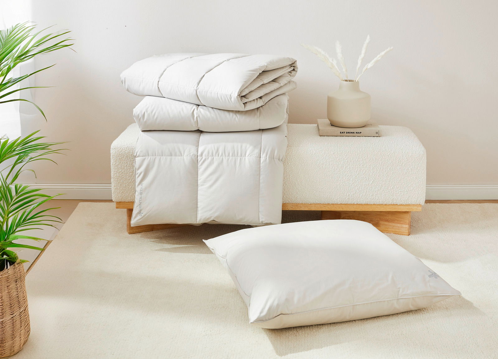 Perspektive auf ein gefaltetes weißes Steppbett und ein passendes Kissen, präsentiert auf einer modernen Bank mit Dekoration.