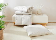 Perspektive auf ein gefaltetes weißes Steppbett und ein passendes Kissen, präsentiert auf einer modernen Bank mit Dekoration.