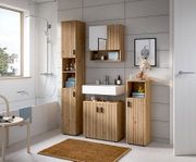 Modernes Badezimmermöbel-Set in Holzoptik mit vertikaler Lamellenfront, Hochschrank, Waschtischunterschrank und Spiegelschrank über weißem Waschbecken, fotografiert in frontaler Perspektive mit leichter Seitenansicht.