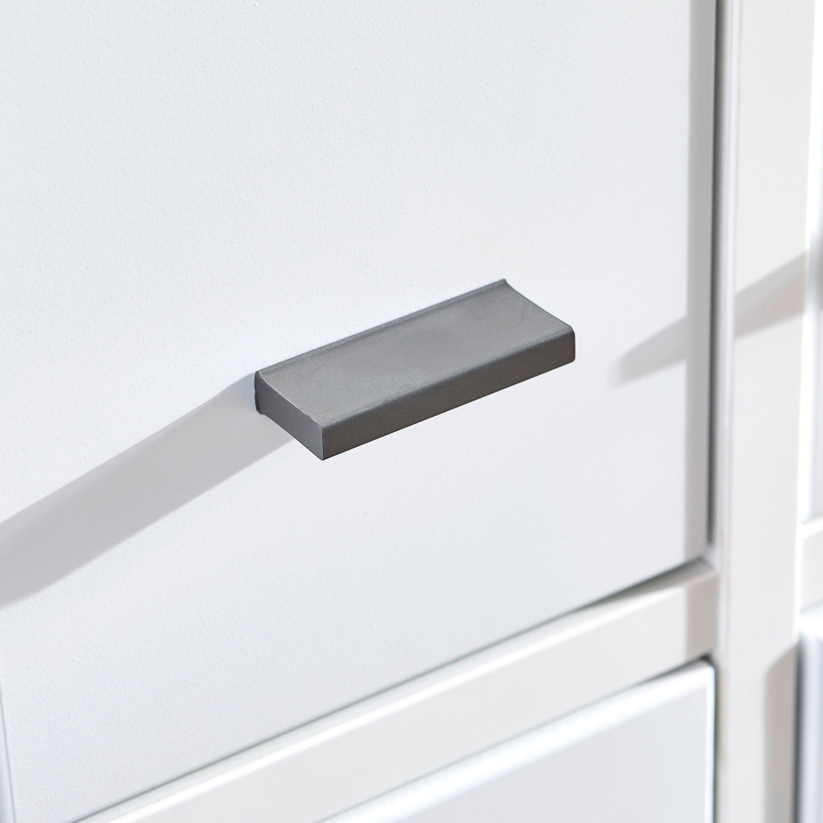 Nahaufnahme eines modernen, grauen Griffs an einer weißen Bürokombination.