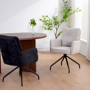Twee schommelstoelen in een moderne ruimte, de ene bekleed met lichte stof en de andere met donkere stof, met een ronde houten tafel en planten op de achtergrond. Aanzicht vanaf de zijkant.