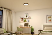 Runde LED-Deckenleuchte in Schwarz mit warmweißem Licht, an der Zimmerdecke montiert, Ansicht von unten in einem modern eingerichteten Schlafzimmer/Homeoffice