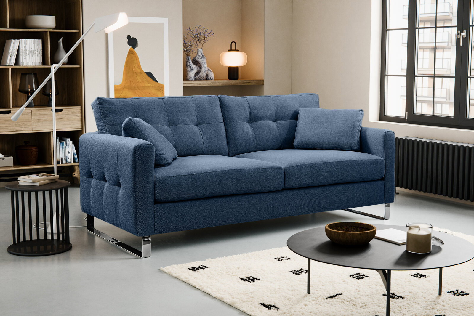 MID.YOU HERA 2,5-zitsbank Blaues 3-Sitzer-Stoffsofa mit gesteppter Rückenlehne, zwei Kissen und verchromten Metallfüßen im modernen Wohnzimmer, Ansicht schräg von vorne.