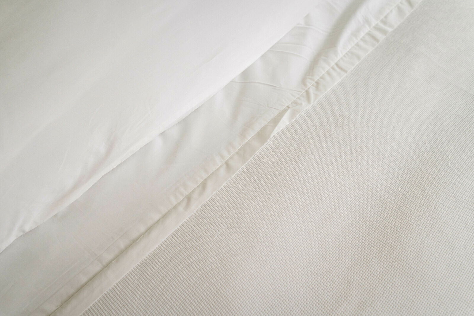 Nahaufnahme einer weißen Bettwäsche mit glatter Textur und dezenter Struktur, von oben fotografiert.