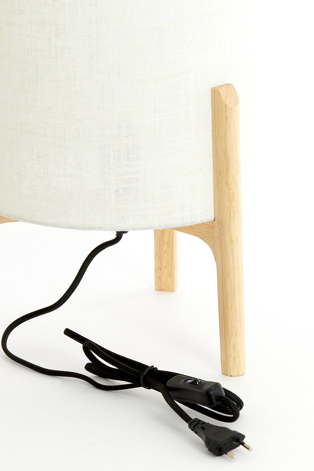 Nahaufnahme einer Tischleuchte mit hellem Stoffschirm und Holzbeinen, seitliche Perspektive, mit schwarzem Kabel und Schalter.
