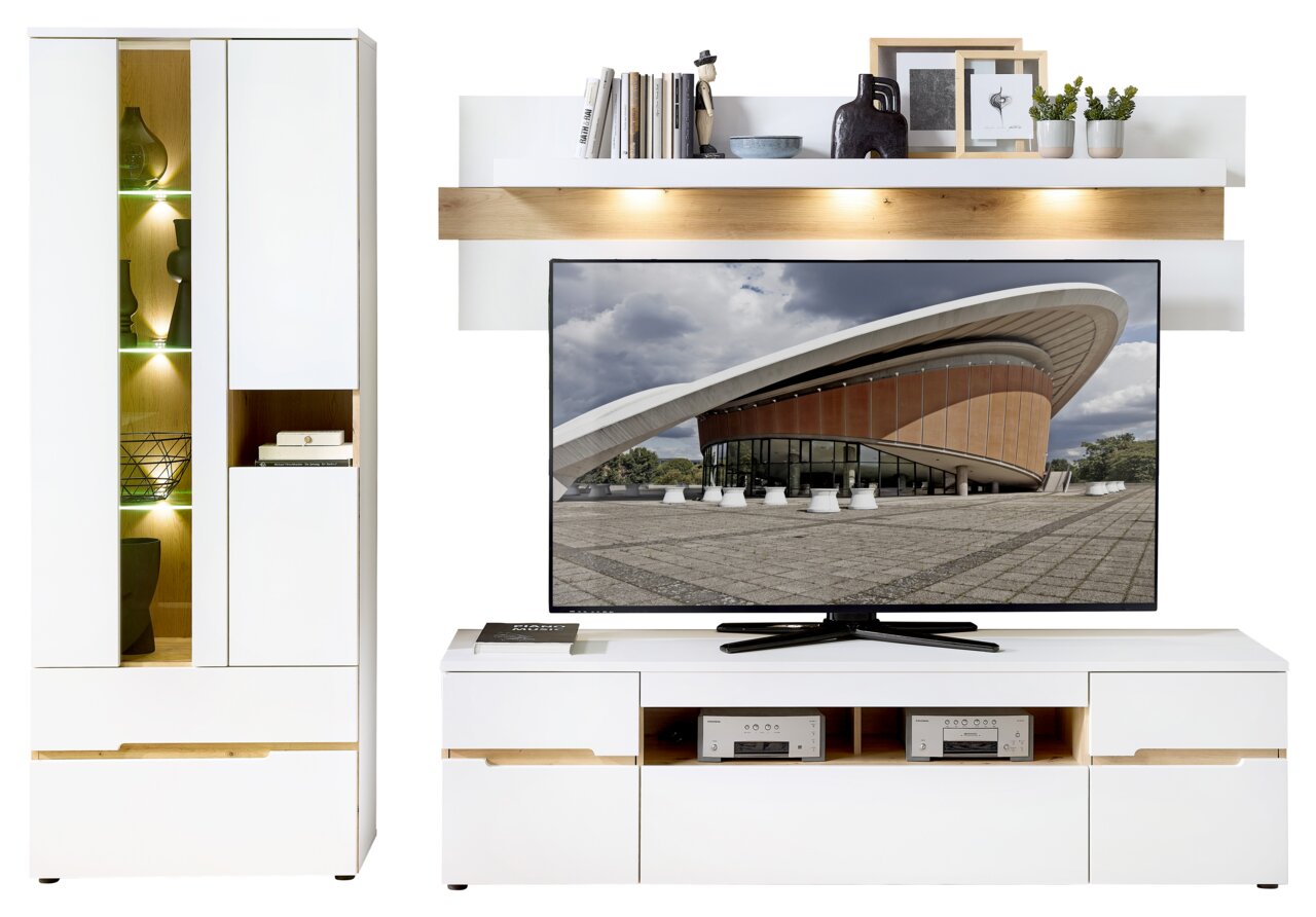 Moderne Wohnwand mit weißem Hochglanz-Finish, bestehend aus einem beleuchteten Vitrinenschrank, einem TV-Board mit großem Flachbildfernseher und einem Wandregal mit Dekorationen, frontal betrachtet.