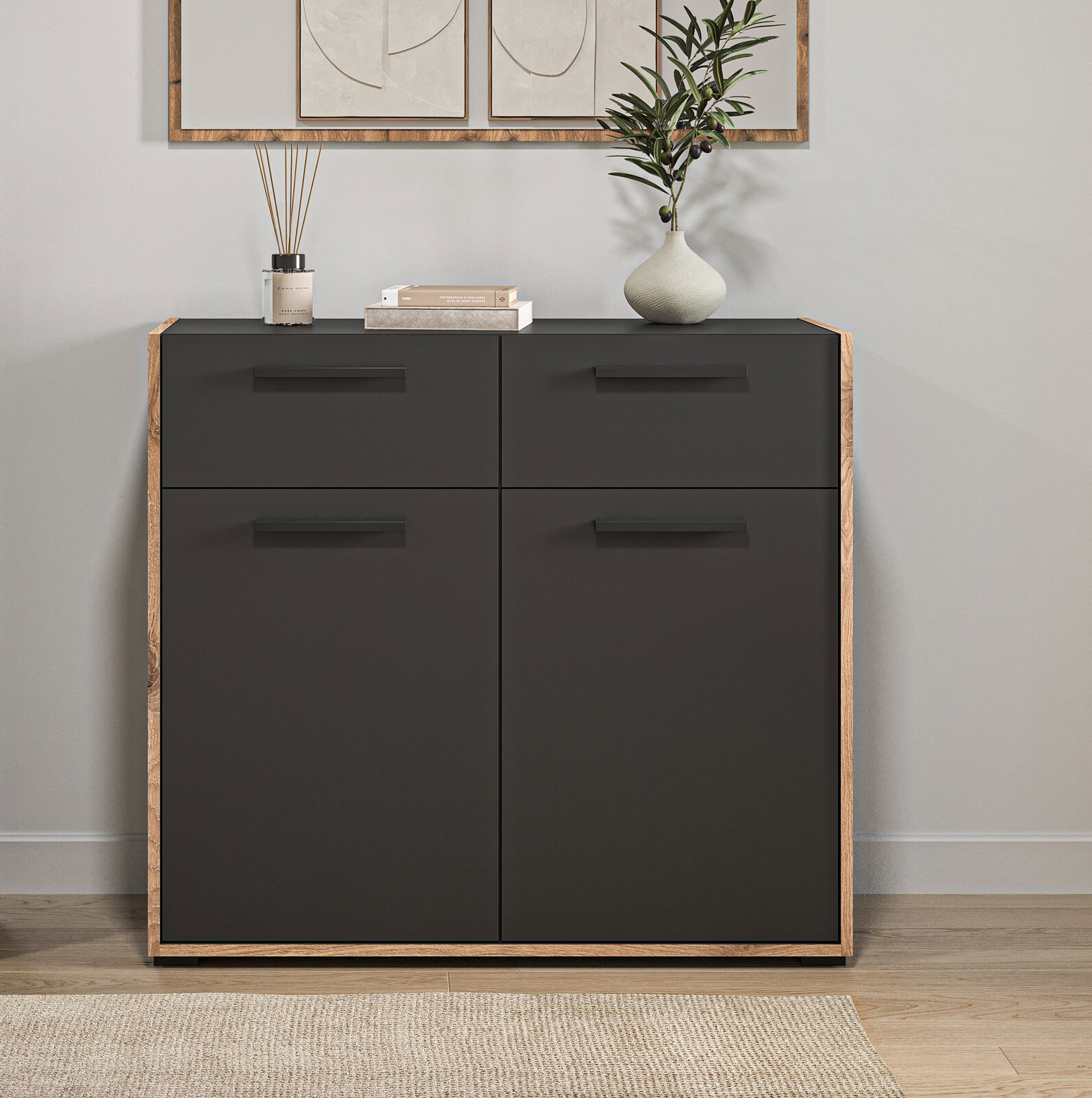Moderne Kommode in Schwarz mit Holzrahmen und vier grifflosen Fronten, dekoriert mit Vase, Büchern und Diffuser, frontal aus Augenhöhe fotografiert.