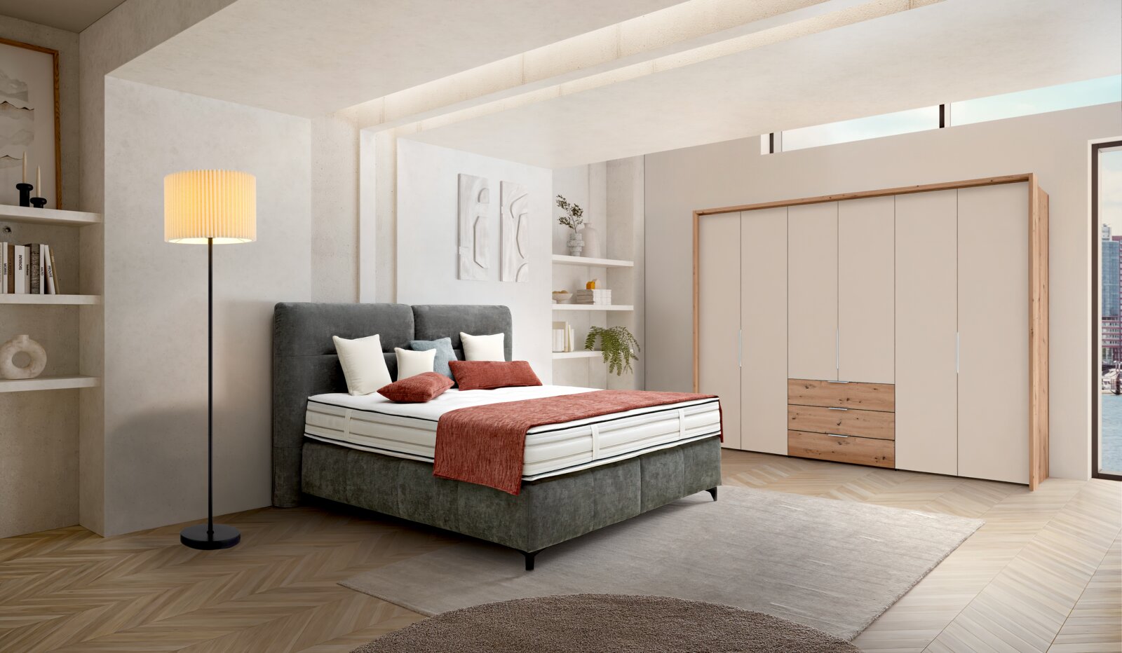 Modernes Schlafzimmer mit grauem Polsterbett und hohem Kopfteil, weißer Matratze und roter Tagesdecke rechts großer Kleiderschrank in Beige mit Holzdetails, aufgenommen in Frontansicht mit leichter Perspektive von links.