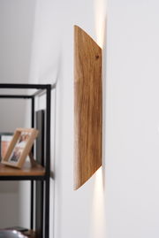 Seitliche Ansicht einer LED-Wandleuchte aus Holz mit warmem Lichtstrahl an einer weißen Wand.