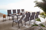 Modernes Garten-Ess-Set mit großem rechteckigem Tisch und acht grauen Hochlehner-Stühlen auf einer Terrasse am Pool, gedeckt mit Geschirr; Perspektive: leicht erhöhte schräge Seitenansicht von vorn rechts.