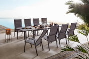 Modernes Garten-Ess-Set mit großem rechteckigem Tisch und acht grauen Hochlehner-Stühlen auf einer Terrasse am Pool, gedeckt mit Geschirr; Perspektive: leicht erhöhte schräge Seitenansicht von vorn rechts.