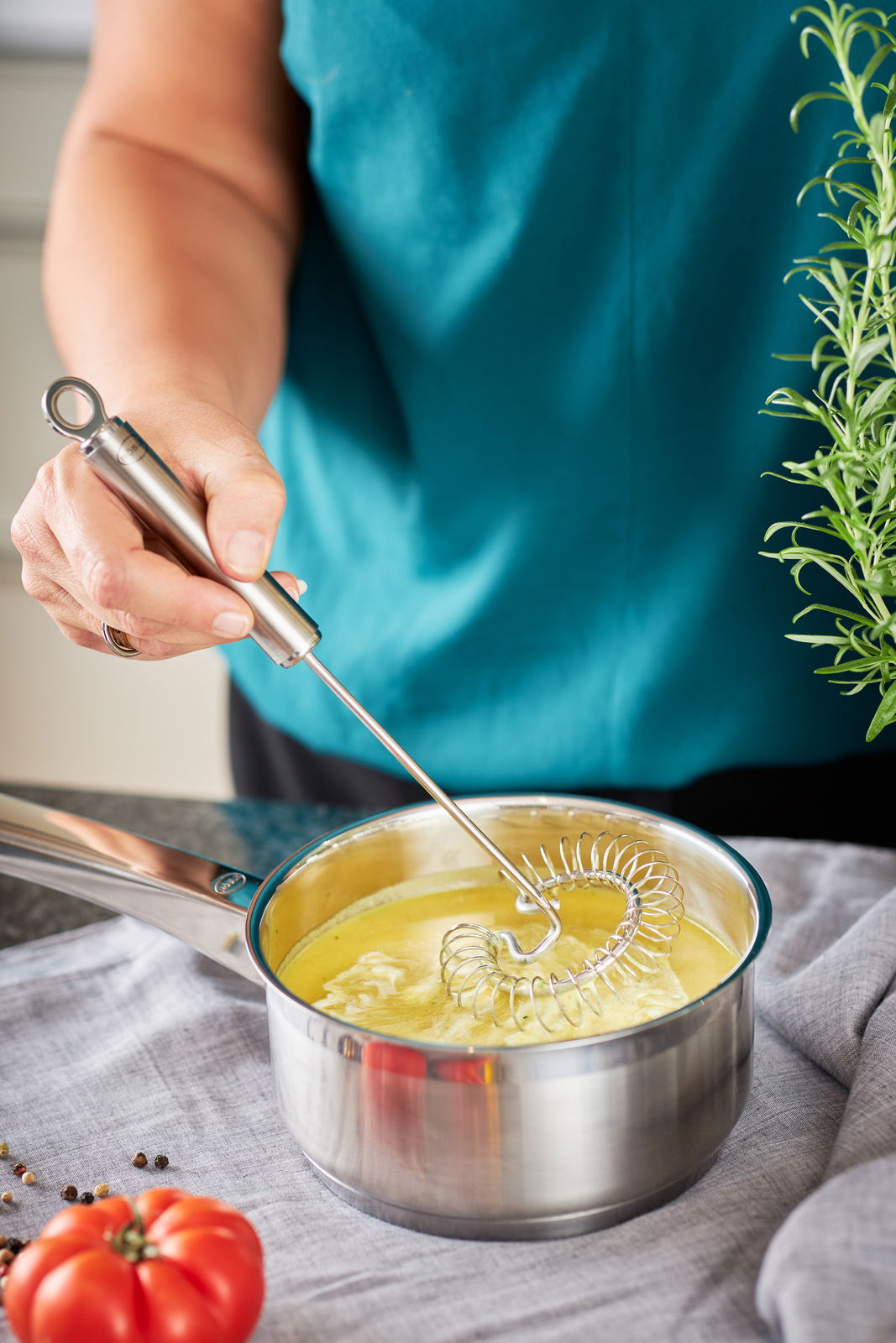 Spiralbesen in einem Topf mit gelber Flüssigkeit, von oben betrachtet, mit einer Hand, die den Besen hält.