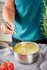 Spiralbesen in einem Topf mit gelber Flüssigkeit, von oben betrachtet, mit einer Hand, die den Besen hält.