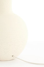 Nahaufnahme eines cremefarbenen Lampenfußes mit gesprenkelter Textur und einem Kabel, das aus der Basis herausführt.