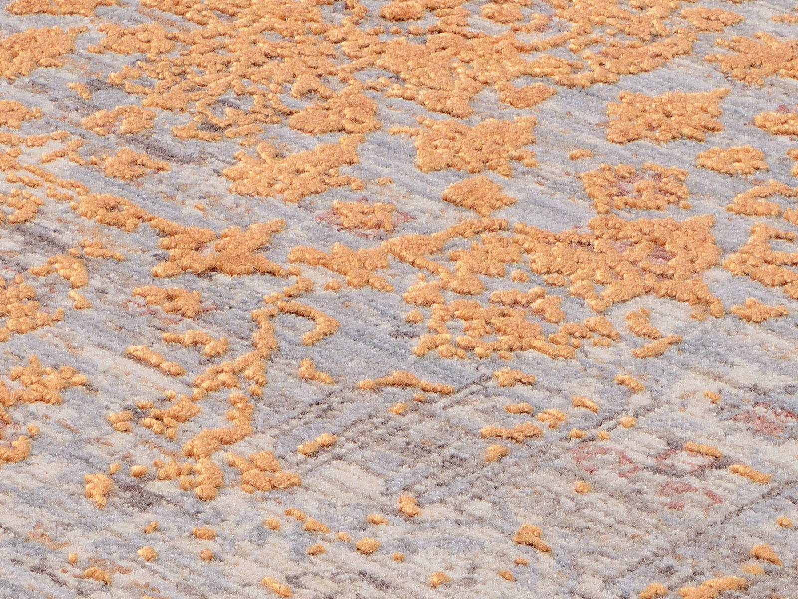 Nahaufnahme eines Designer Teppichs mit abstraktem Muster in Orange- und Grautönen, seitliche Perspektive