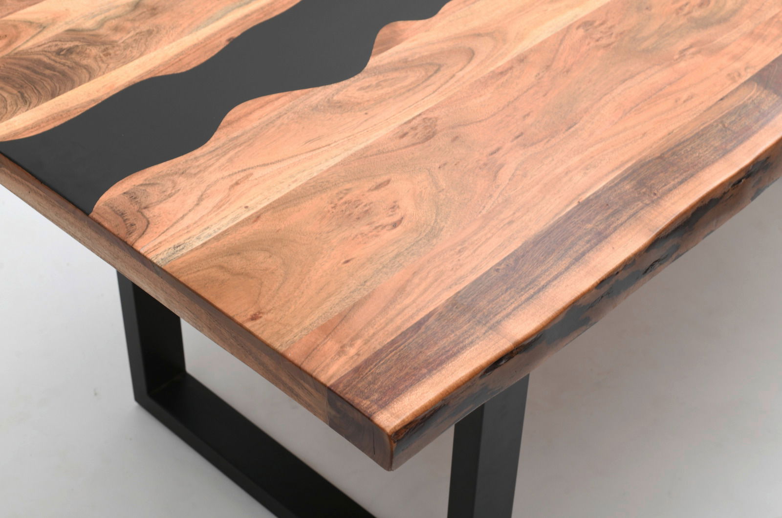 Nahaufnahme eines Esstisches mit einer Tischplatte aus Holz und schwarzem Harz, mit Metallbeinen, aus der Perspektive von oben.