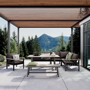 Moderne Outdoor-Lounge mit Ecksofa, Sessel, Esstisch und Bank unter Holz-Lamellen-Pergola auf Terrasse, frontal aus leicht niedriger Perspektive mit Berg- und Waldpanorama im Hintergrund