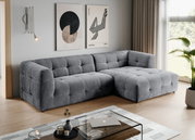 Modernes graues, gepolstertes Ecksofa mit rechter Ottomane und quadratischer Steppung im Wohnzimmer, fotografiert in schräger Frontansicht von links.