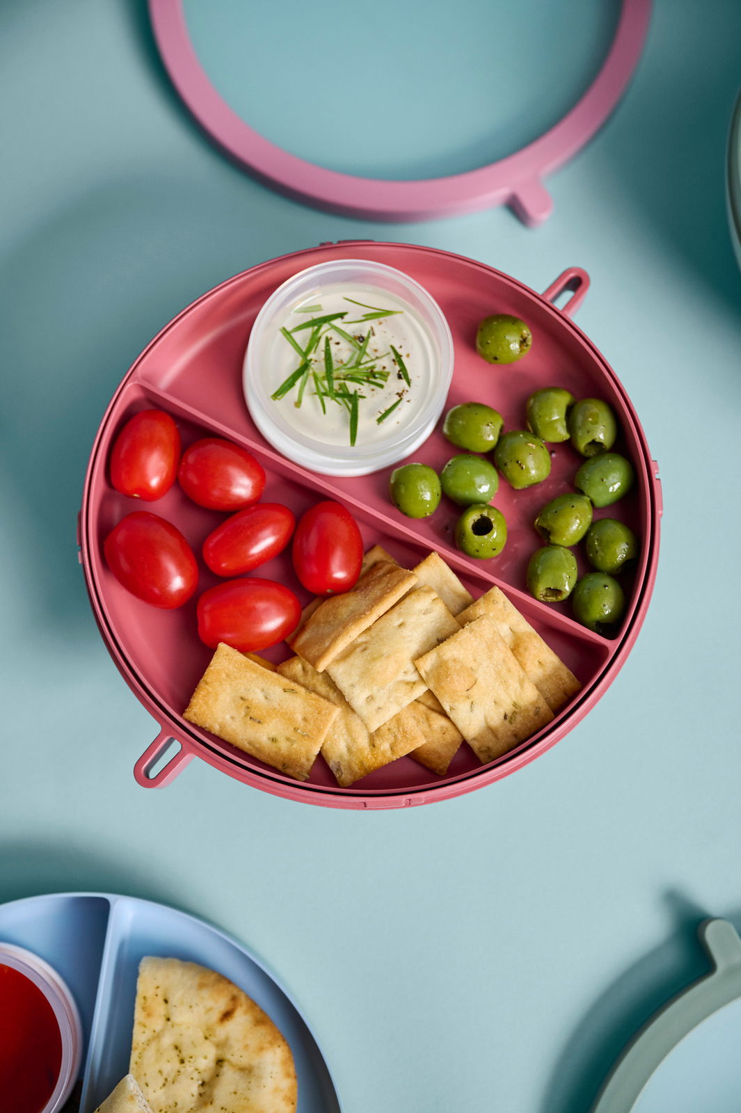 Lunchbowl in Vivid Mauve von oben mit Tomaten, Oliven, Crackern und Dip.