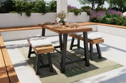 Moderner Gartentisch mit Holzplatte und schwarzen Metallbeinen, umgeben von gepolsterten Bänken, auf einer Terrasse mit Pflanzen im Hintergrund. Perspektive von schräg vorne.
