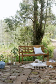 Holzgartenbank mit Kissen, umgeben von Natur, aus seitlicher Perspektive fotografiert.