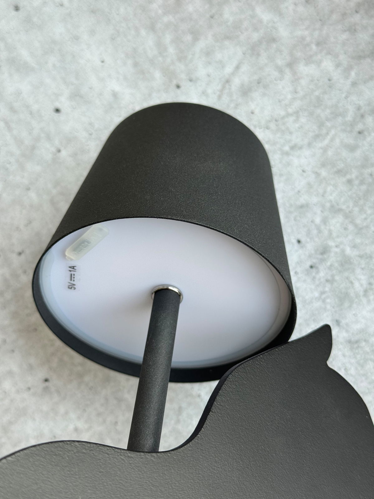 Schwarze Akku-Tischleuchte von unten fotografiert, zeigt den Lampenschirm und den Ständer auf grauem Hintergrund.