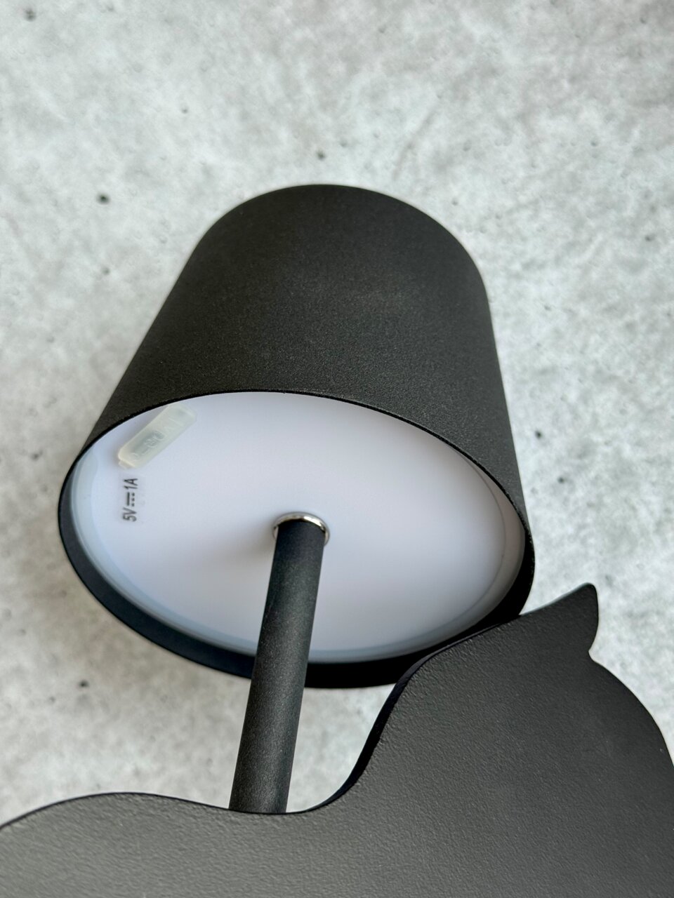 Schwarze Akku-Tischleuchte von unten fotografiert, zeigt den Lampenschirm und den Ständer auf grauem Hintergrund.