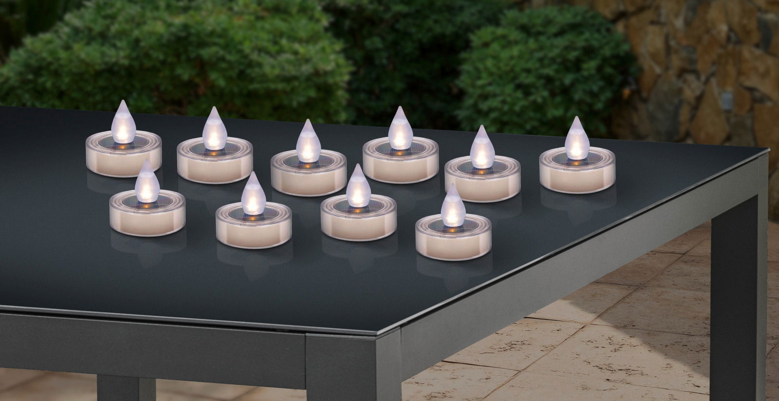 Ambia Garden Solarleuchte AMARILLO Mehrere runde Solarleuchten in Kerzenform auf einem Tisch im Freien, seitliche Perspektive.