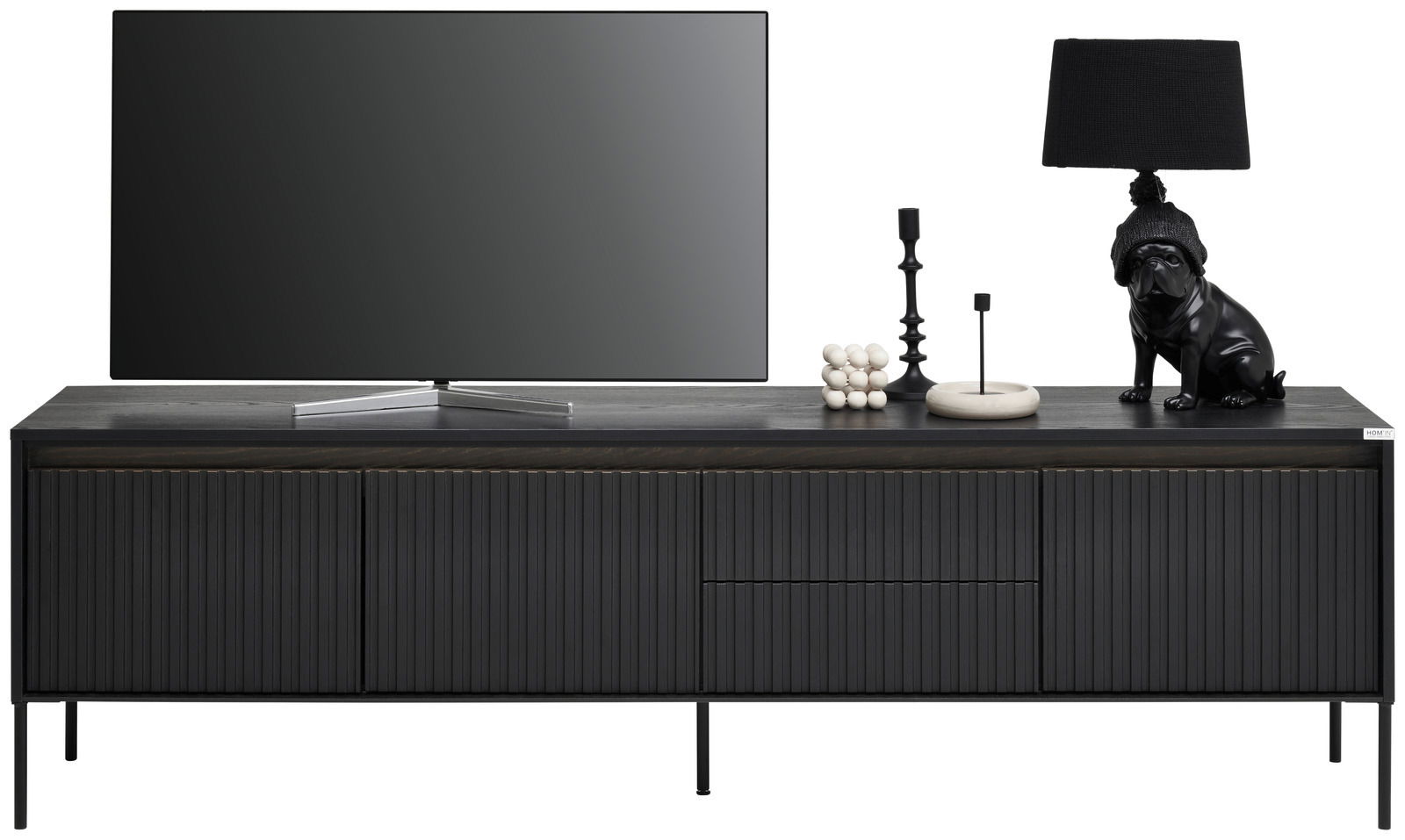 Frontale Ansicht eines modernen, schwarzen TV-Lowboards mit gerillten Türen, dekoriert mit einem Fernseher, einer Lampe und Dekorationsobjekten.