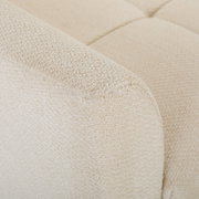 Detailaufnahme aus schräger Nahperspektive: cremefarbener Bouclé-Stoffbezug eines gepolsterten Sofas mit abgerundeter Armlehne und gestepptem Sitzpolster