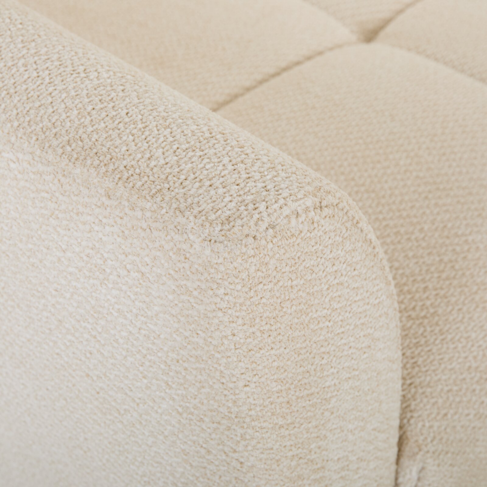 Detailaufnahme aus schräger Nahperspektive: cremefarbener Bouclé-Stoffbezug eines gepolsterten Sofas mit abgerundeter Armlehne und gestepptem Sitzpolster