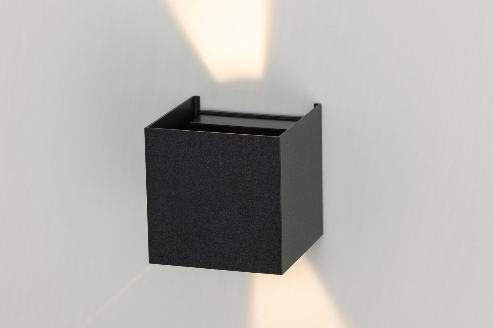 Schwarze LED-Wandleuchte in quadratischer Form, die sowohl nach oben als auch nach unten Licht abstrahlt. Perspektive von vorne leicht seitlich.