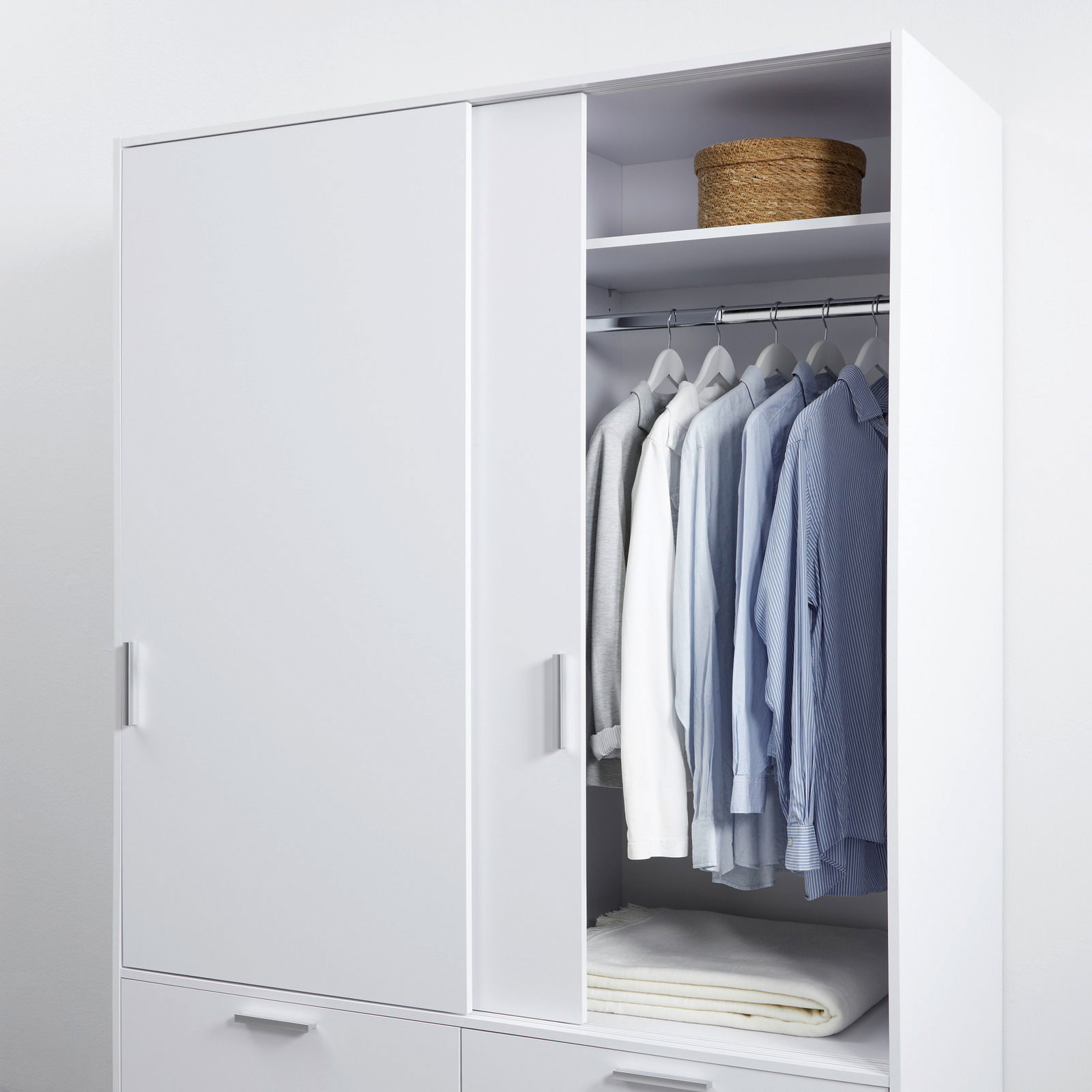 Weißer, zweitüriger Schiebetürenschrank mit geöffneter Tür, zeigt hängende Hemden und ein Fach mit einem Korb, aus frontaler Perspektive.
