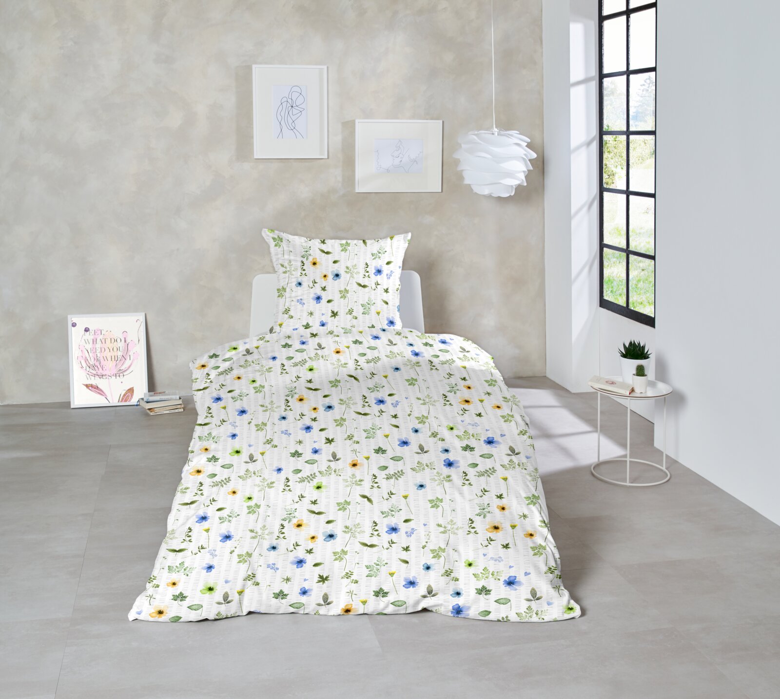 Einzelbett mit weißer Bettwäsche mit Blumen- und Blättermuster in Blau, Gelb und Grün, frontal aus leicht erhöhter Perspektive im hellen Schlafzimmer inszeniert