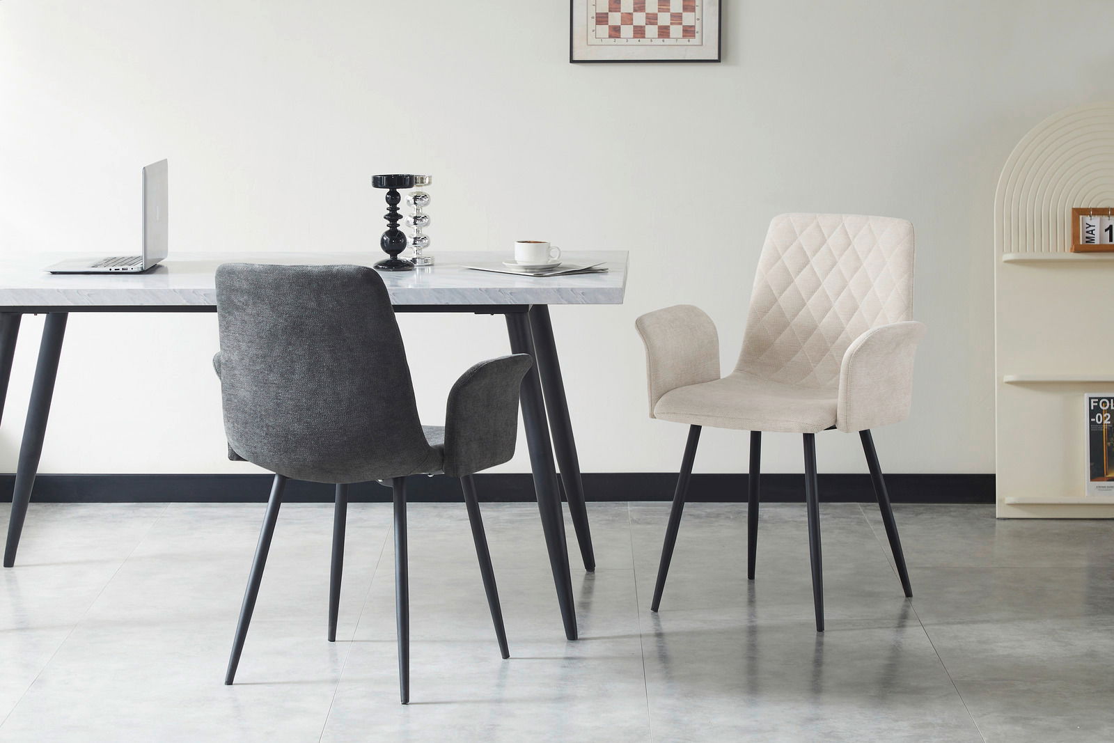 Zwei Armlehnstühle in einem modernen Esszimmer, einer in dunklem Grau und der andere in hellem Beige, mit einem Tisch im Hintergrund. Perspektive von vorne.