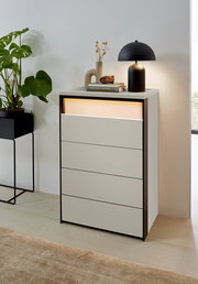 Hochkommode mit vier Schubladen, dekoriert mit einer Lampe und Büchern, aus einer seitlichen Perspektive fotografiert.