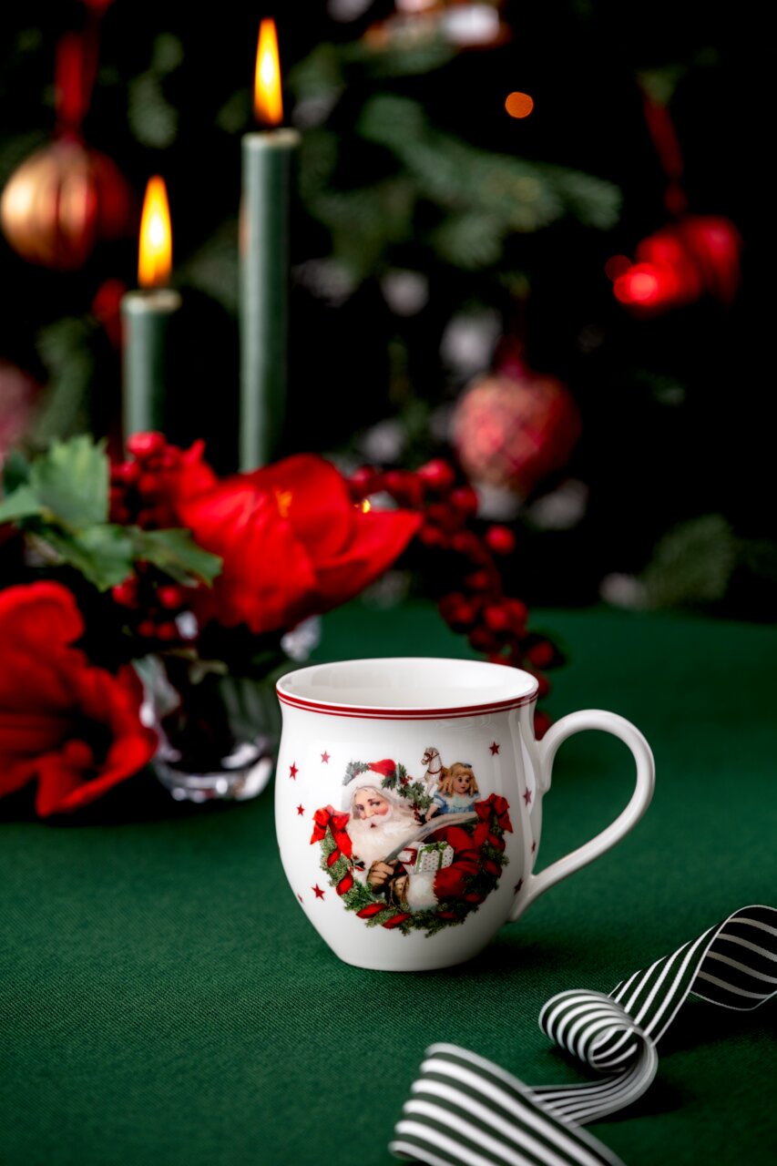 Weihnachtlicher Henkelbecher mit Santa Claus-Motiv, umgeben von festlicher Dekoration, aus seitlicher Perspektive fotografiert.