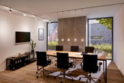 Moderne kantoorverlichting met kabelophanging, zijaanzicht op een vergadertafel met vijf stoelen en grote ramen op de achtergrond.