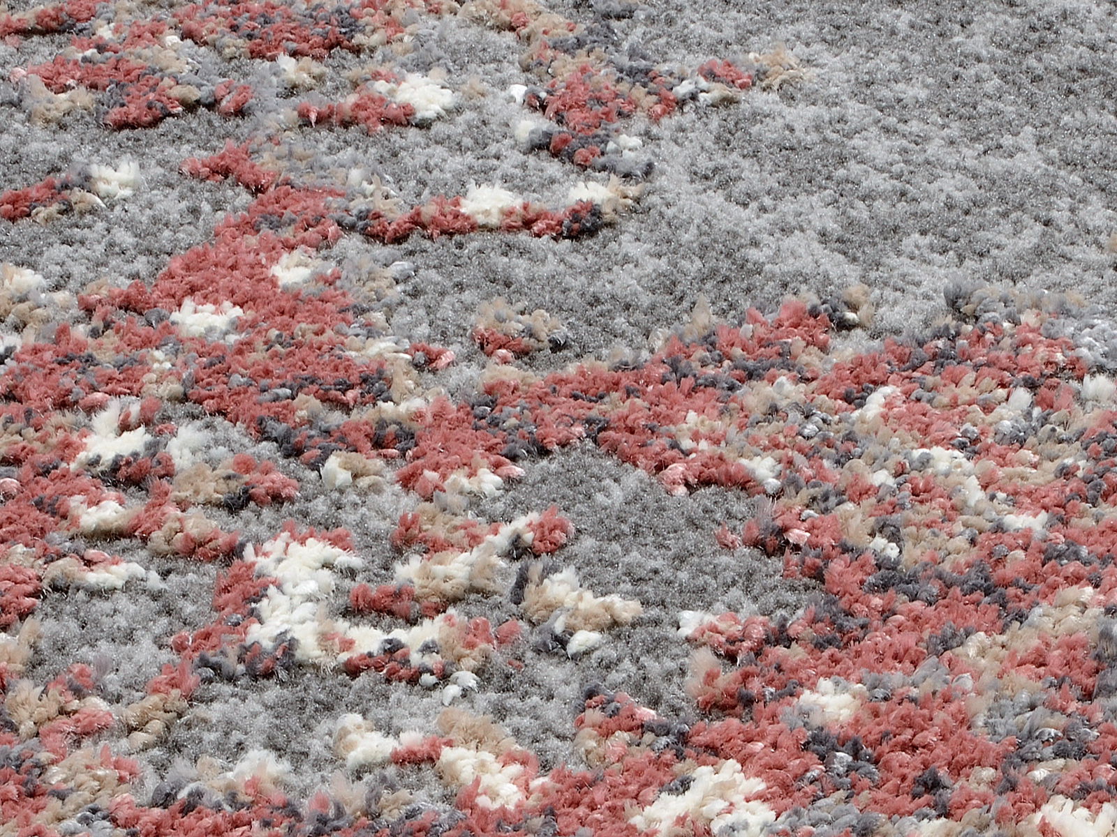 Nahaufnahme eines Designer-Teppichs mit flauschiger Textur in Grau-, Rot- und Beigetönen, aus seitlicher Perspektive aufgenommen.