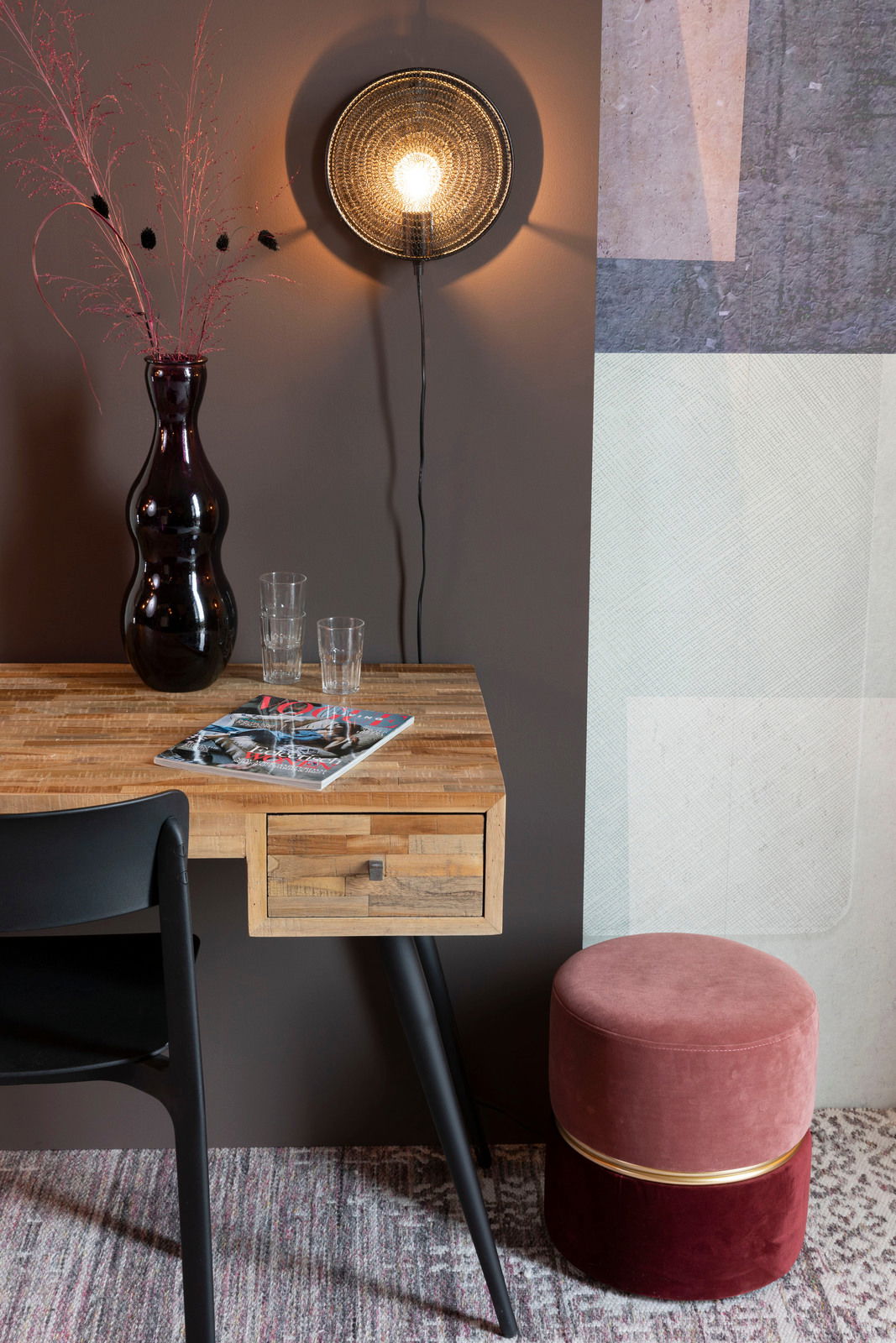 Runder, zweifarbiger Hocker in Rosa und Rot mit goldener Zierleiste, seitlich neben einem Holztisch mit schwarzem Stuhl platziert.