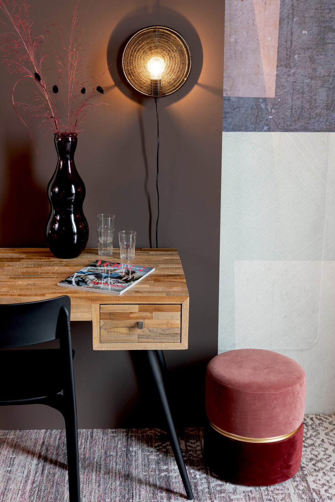 Runder, zweifarbiger Hocker in Rosa und Rot mit goldener Zierleiste, seitlich neben einem Holztisch mit schwarzem Stuhl platziert.