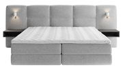 Frontale Ansicht eines grauen Boxspringbetts mit gepolstertem Kopfteil, integrierten Nachttischen und Wandlampen.