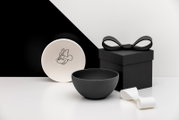 Schwarz-weißes Schalen-Set mit Minnie-Maus-Motiv, daneben schwarze Geschenkbox mit Schleife und weißes Band, aufgenommen in leichter Seitenansicht (3/4-Perspektive) vor minimalistischem Hintergrund.
