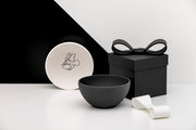 Schwarz-weißes Schalen-Set mit Minnie-Maus-Motiv, daneben schwarze Geschenkbox mit Schleife und weißes Band, aufgenommen in leichter Seitenansicht (3/4-Perspektive) vor minimalistischem Hintergrund.