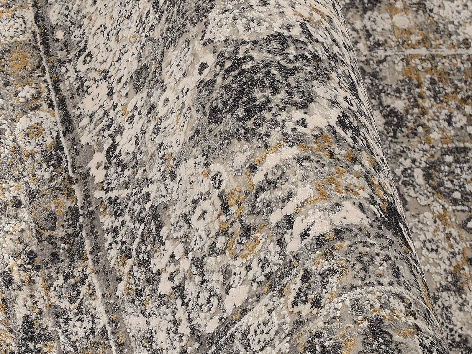 Nahaufnahme eines Designer-Teppichs mit abstraktem Muster in Grau-, Beige- und Goldtönen, aus seitlicher Perspektive aufgenommen.